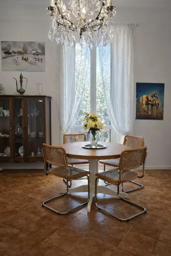 Dining corner with round table, chandelier and tall window.