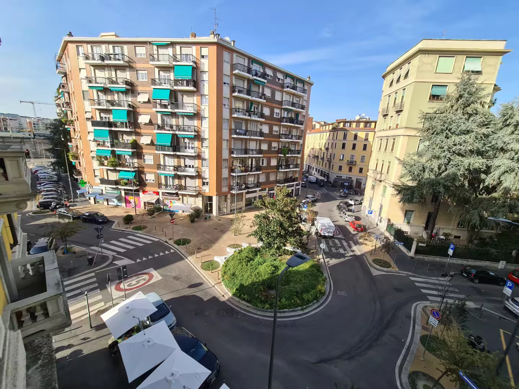 Wide view across a NoLo roundabout with surrounding Milan buildings and open sky.
